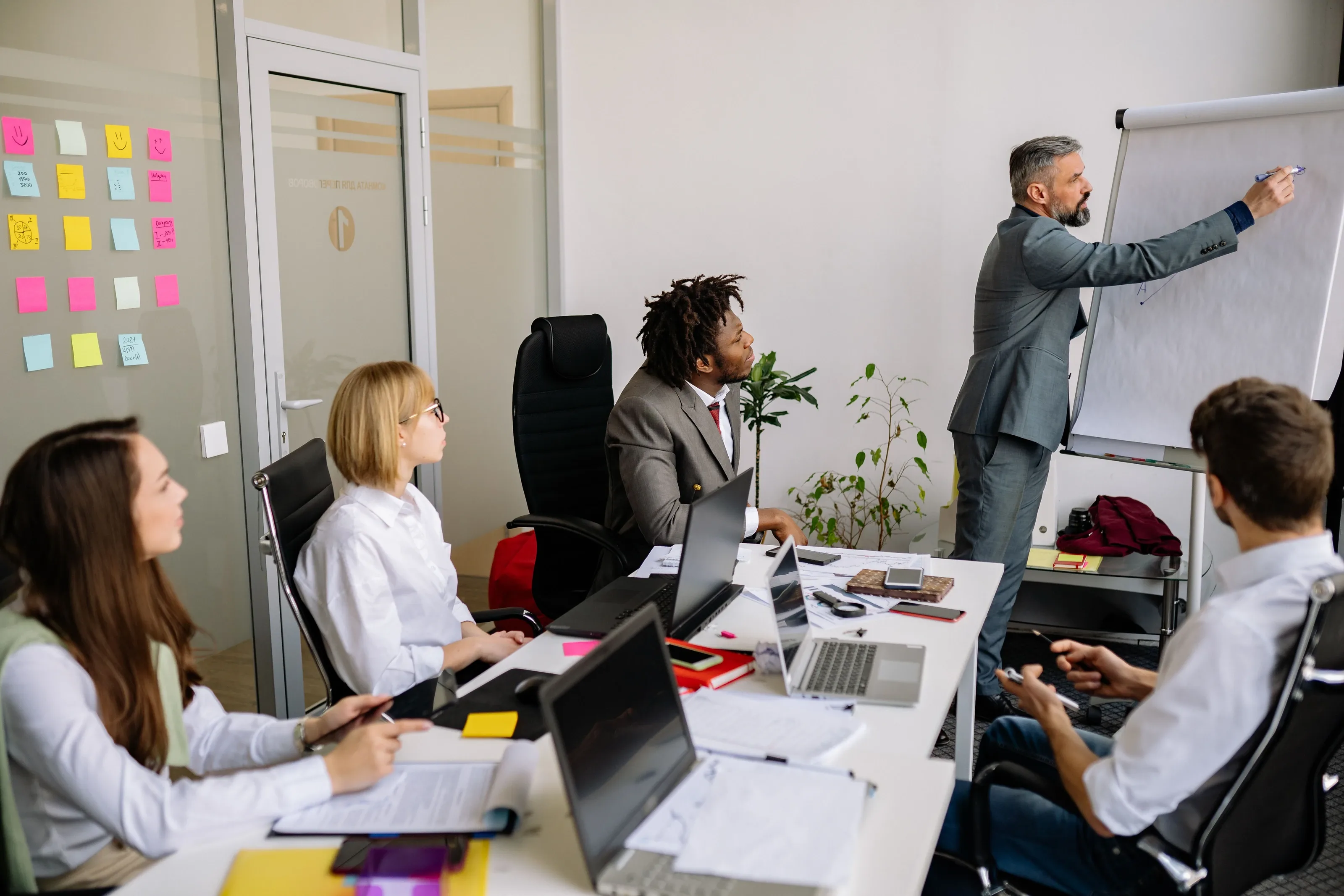 Trainer writing on a flip chart while a group of delegates takes notes in a training room