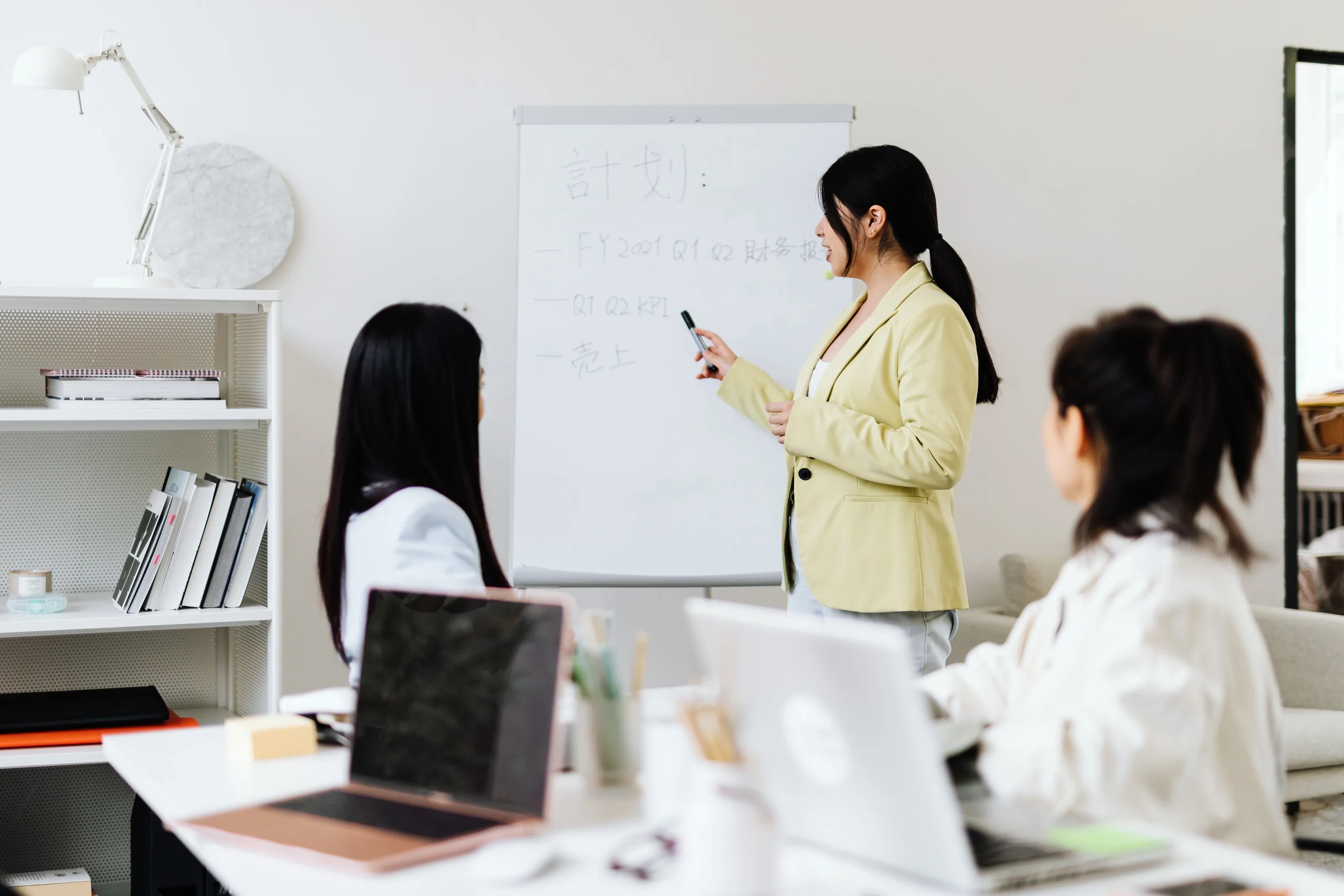 Tutor explaining notes on a whiteboard to a small class working on laptops